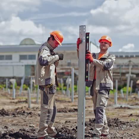 construction the solar power plant. engineering team in orange helmets and uniform working on installing metal basis for future solar farm.