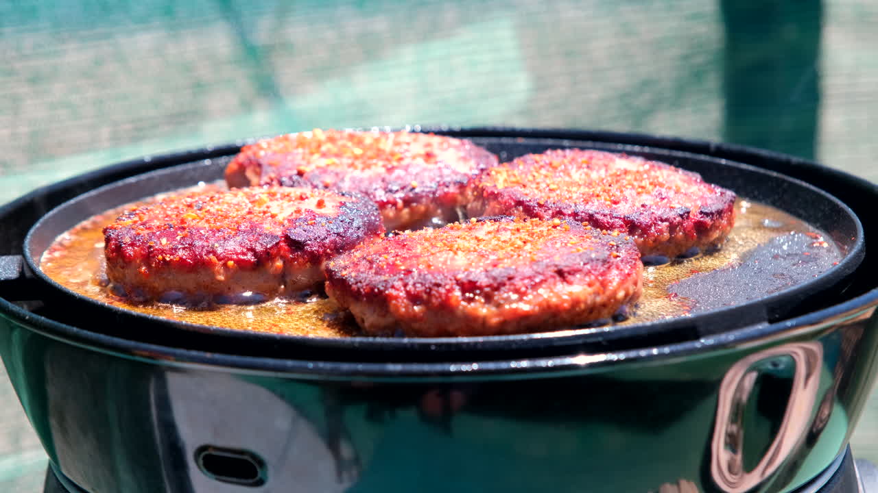 Seitenansicht von saftigen, gewürzten Rindfleischbratlingen, die auf einem Campingplatz in der Pfanne gebraten werden