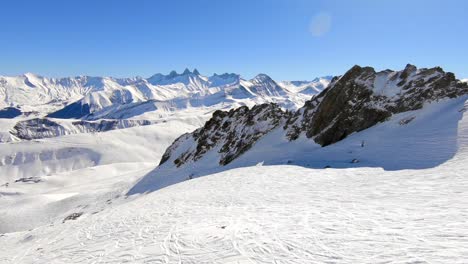 空中拍攝的雪覆蓋的山地風景,前景有岩石形成和滑雪者步道