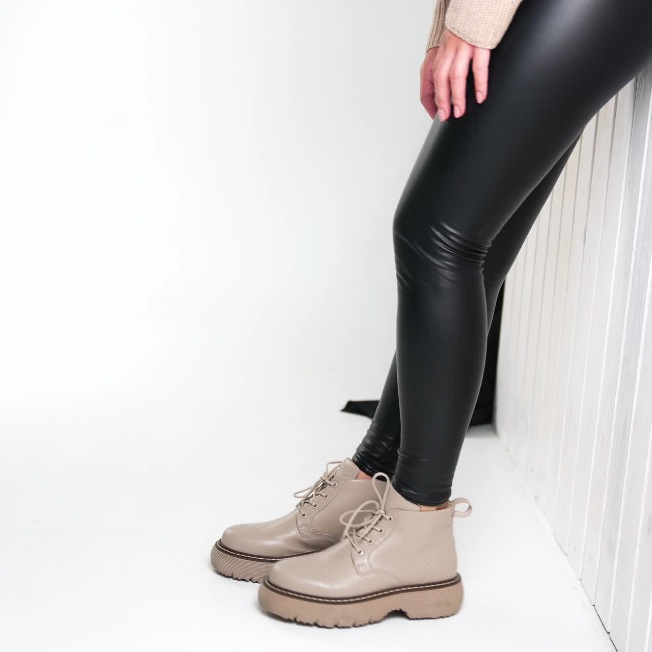 Beautiful lady legs in black leggings and stylish boots. Model demonstrating modern fashionable footwear standing at white wall in studio