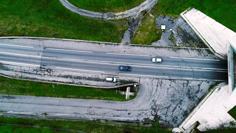 aerial view over highway roads going into a tunnel in france. only grass fields and trees around the roads. cars and trucks driving on the roads.