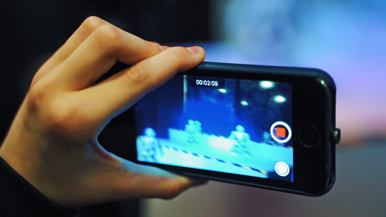 View of man's hand holding a mobile phone and taking pictures of dancing robots.