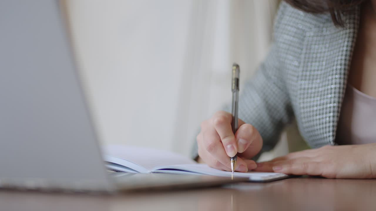 Businesswoman analyzing the graph and typing on laptop. Remote job young female in eyeglasses writes notes in clipboard and typing on laptop keyboard