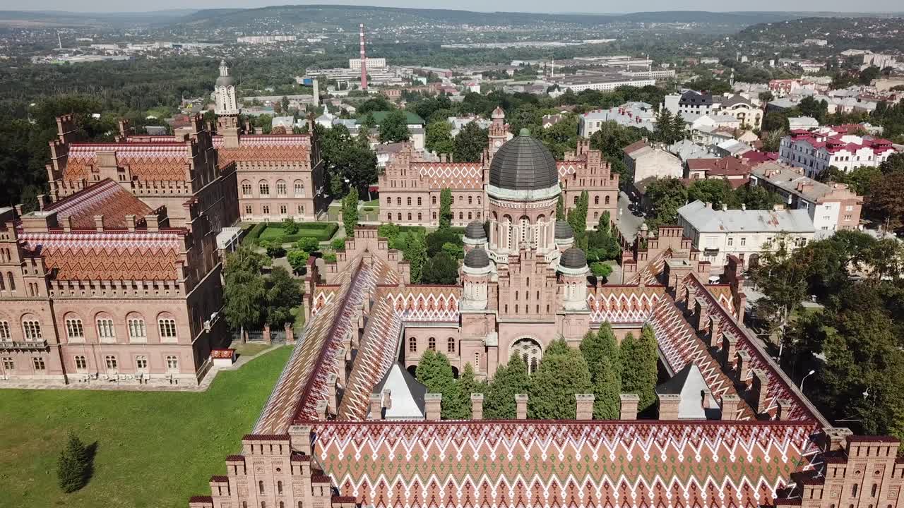 Ukraine,Chernivtsi University's drone footage zooming in towards to the tower and the inner garden and than turns around the building on sunny summer day, clock tower, other towers,roofs,Ukranian flag