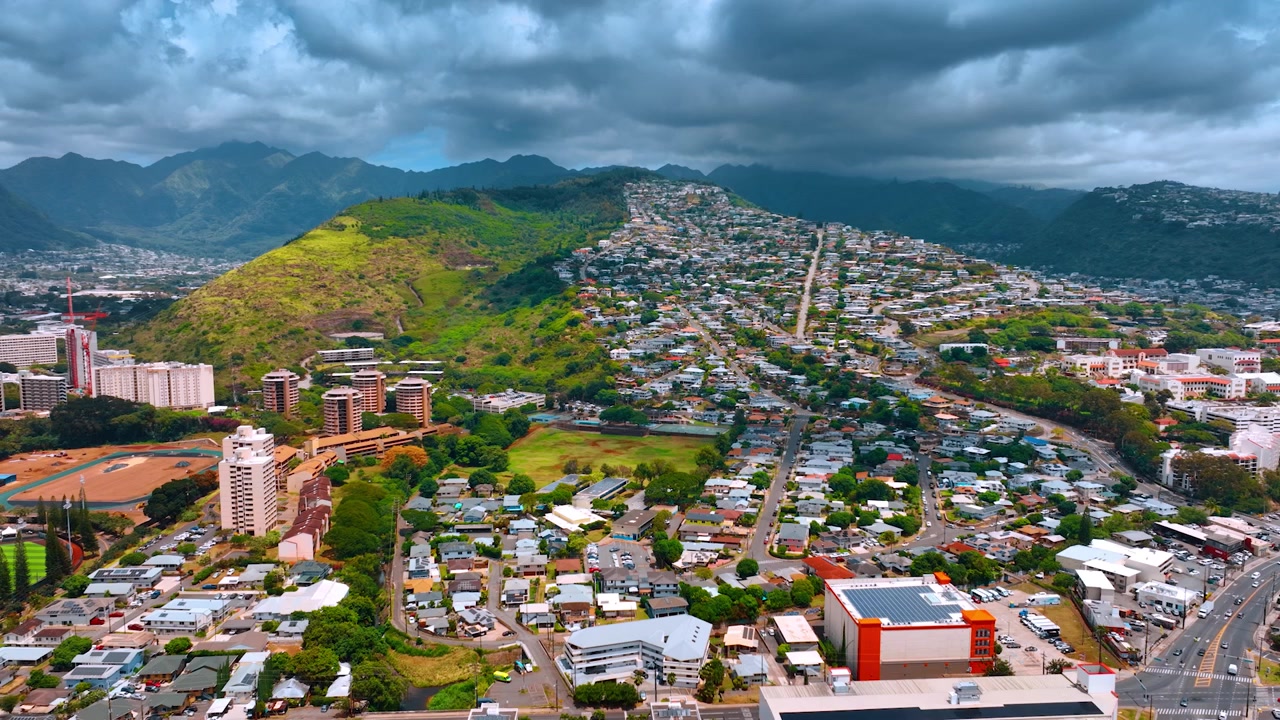 Area residenziale a bassa densità di Honolulu, Oahu, USA. Suggestivo paesaggio di nuvole che si addensa sopra la città e le montagne. Prospettiva aerea