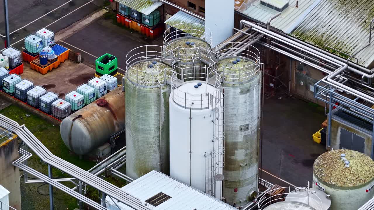 Imagens aéreas capturam tanques de armazenamento e contêineres em um ambiente industrial. Ideal para uso em estudos ambientais ou documentários industriais