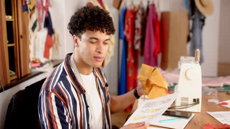 diseñador de moda masculino biracial diseñando ropa en el estudio, en cámara lenta