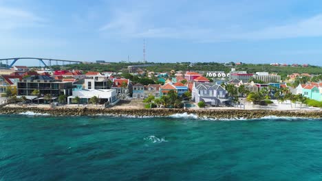 Clear-Caribbean-waters-off-coast-of-Pietermaai-and-Punda-homes-on-coast,-Queen-Juliana-bridge-behind