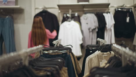 lady walks through a clothing store, heading towards a black hanging item, then moves to observe a white garment, the store has neatly arranged clothes in multiple sections with varied colors