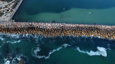 a rocky ocean jetty stretching out into the pacific ocean - aerial tilt down sliding reveal