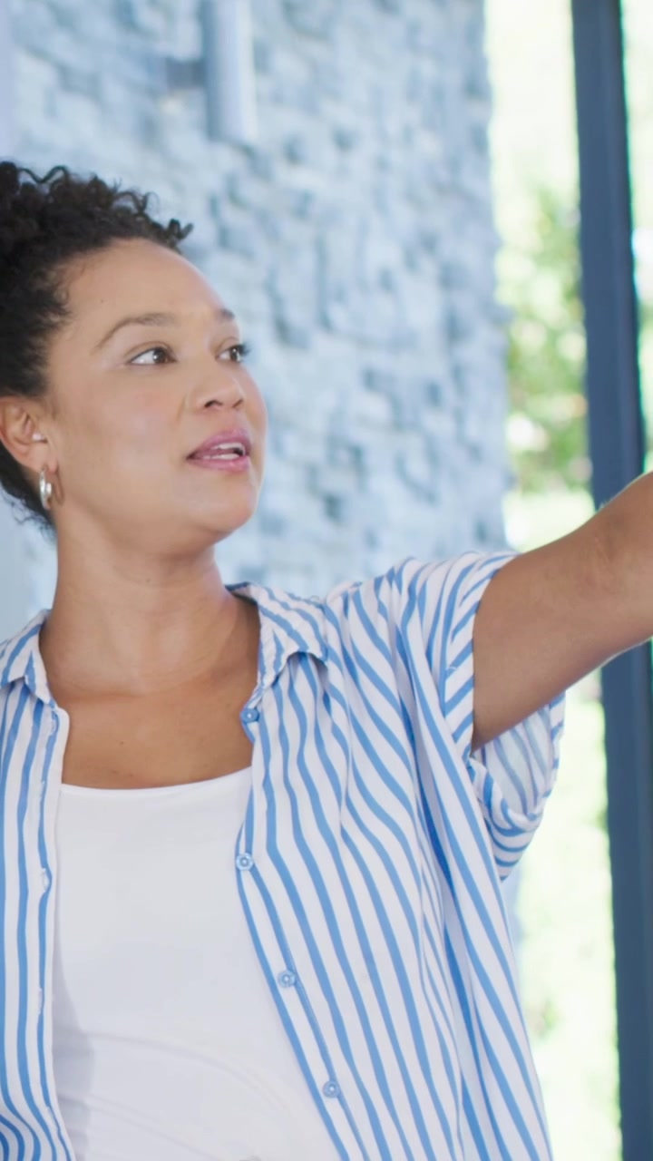 Vertical video: Listening woman nodding, pointing to window as man talking at home, in striped top