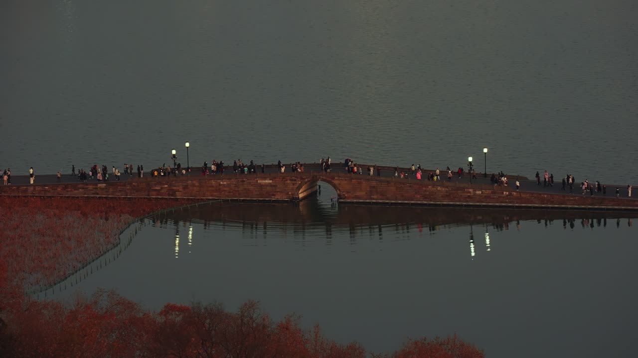 Traditional Arched Stone Bridge and Pedestrians Reflected on West Lake at Dusk
