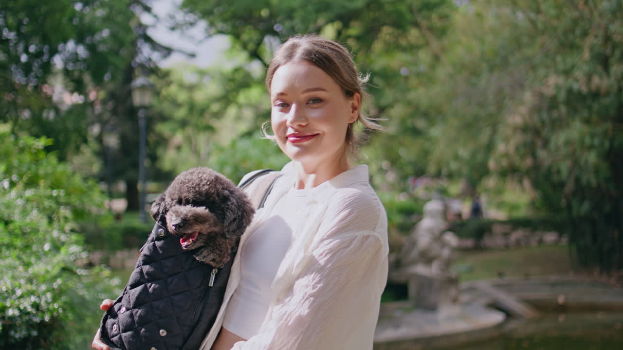 Brunette holding small dog in sunny park closeup. Portrait happy woman with pet