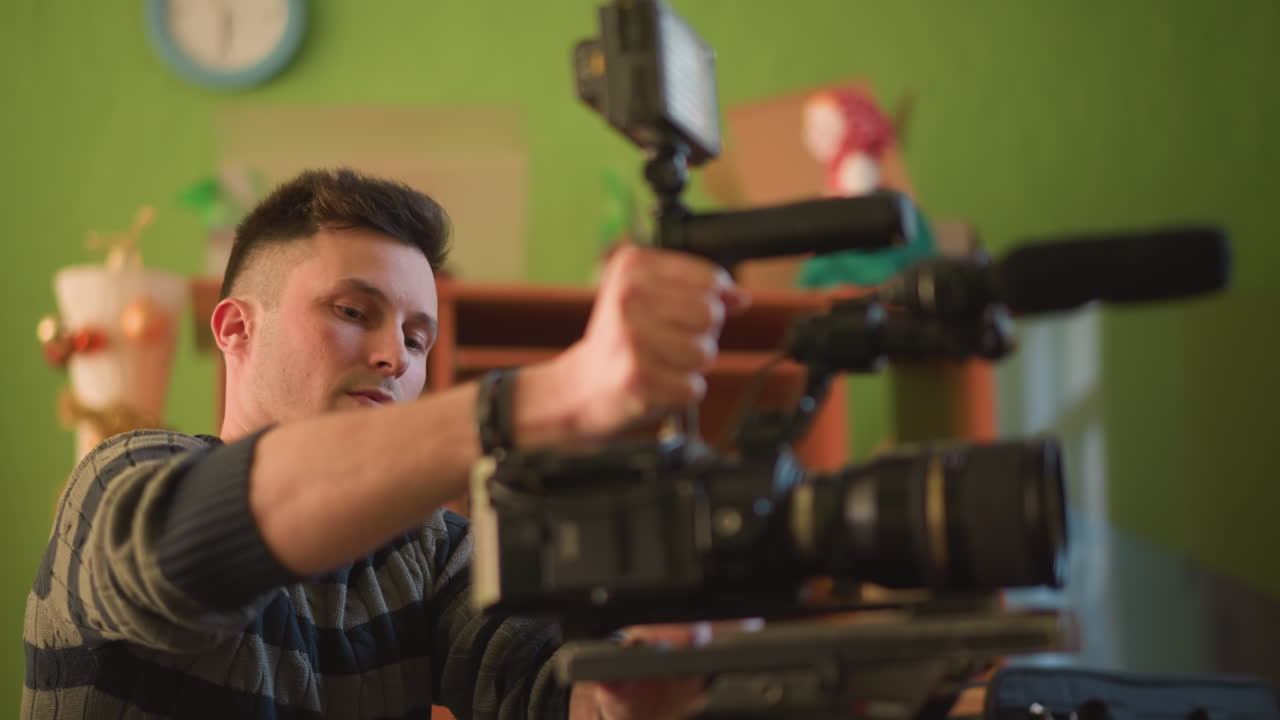 TV technician focused on camera equipment, adjusting lens and microphone setup, green background, working indoors with shelves and door in background