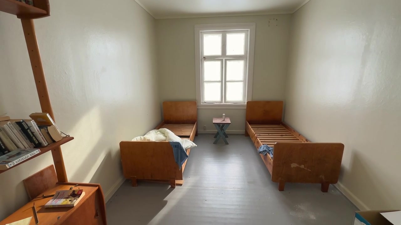Slow panning shot of a small bedroom in a lighthouse with two twin bed frames and a bookshelf and empty boxes.