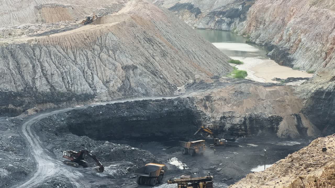 A long shot captures the impressive scale of a mining operation in progress, where a powerful excavator is actively filling a large mining dump truck with coal