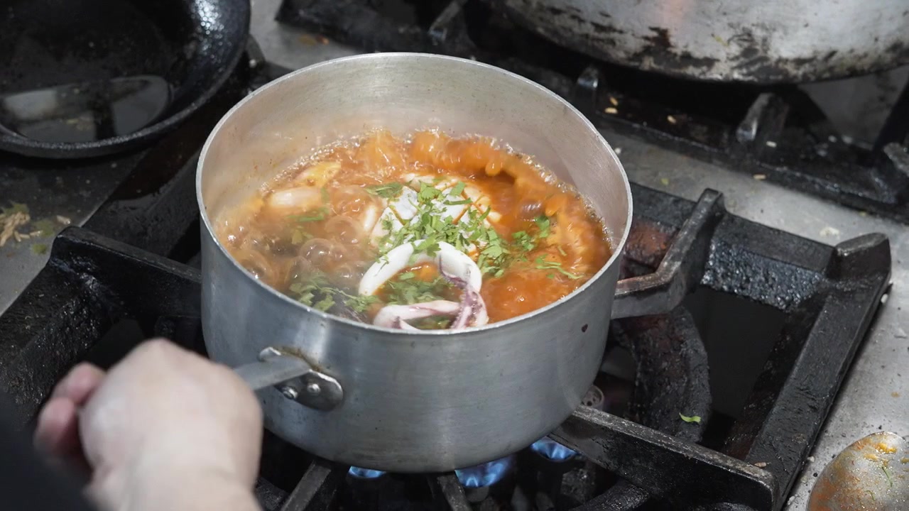 Mano che mescola un piatto peruviano di frutti di mare con calamari e prezzemolo in una casseruola su un fornello a gas