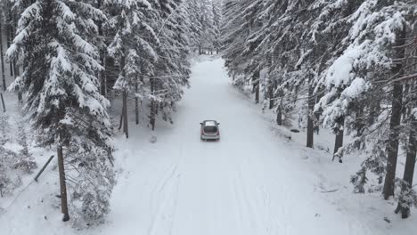 Luftaufnahme-Eines-Sportwagens,-Der-An-Einem-Kalten-Wintertag-Auf-Einer-Verschneiten-Straße-Zwischen-Schneebedeckten-Bäumen-Im-Wald-Fährt---Drohnenaufnahme,-Niedriger-Winkel,-Folgen