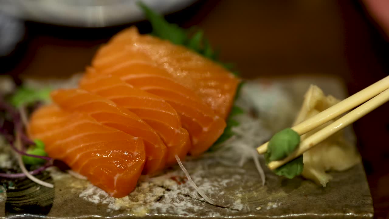 Chopsticks picking wasabi with salmon sashimi