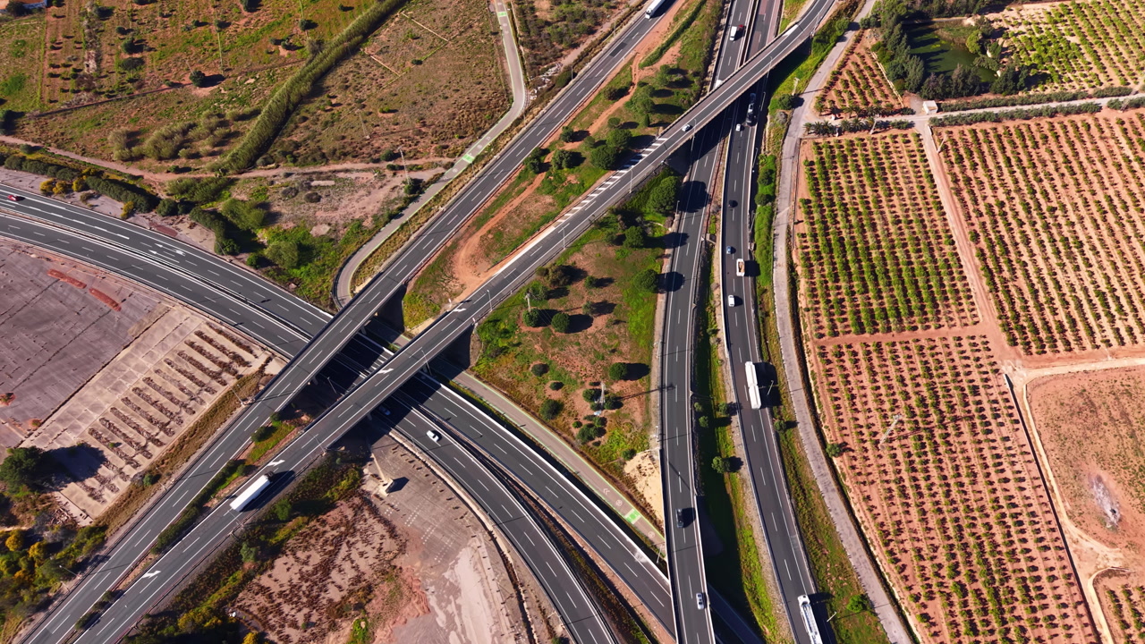Overhead view of a multi-lane highway interchange with vehicles moving through intersecting elevated roads surrounded by farmland and scrubland