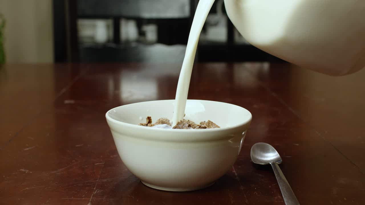 Latte che si versa in una ciotola bianca piena di cereali