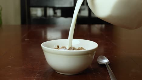 milk pouring into a white bowl filled with cereal