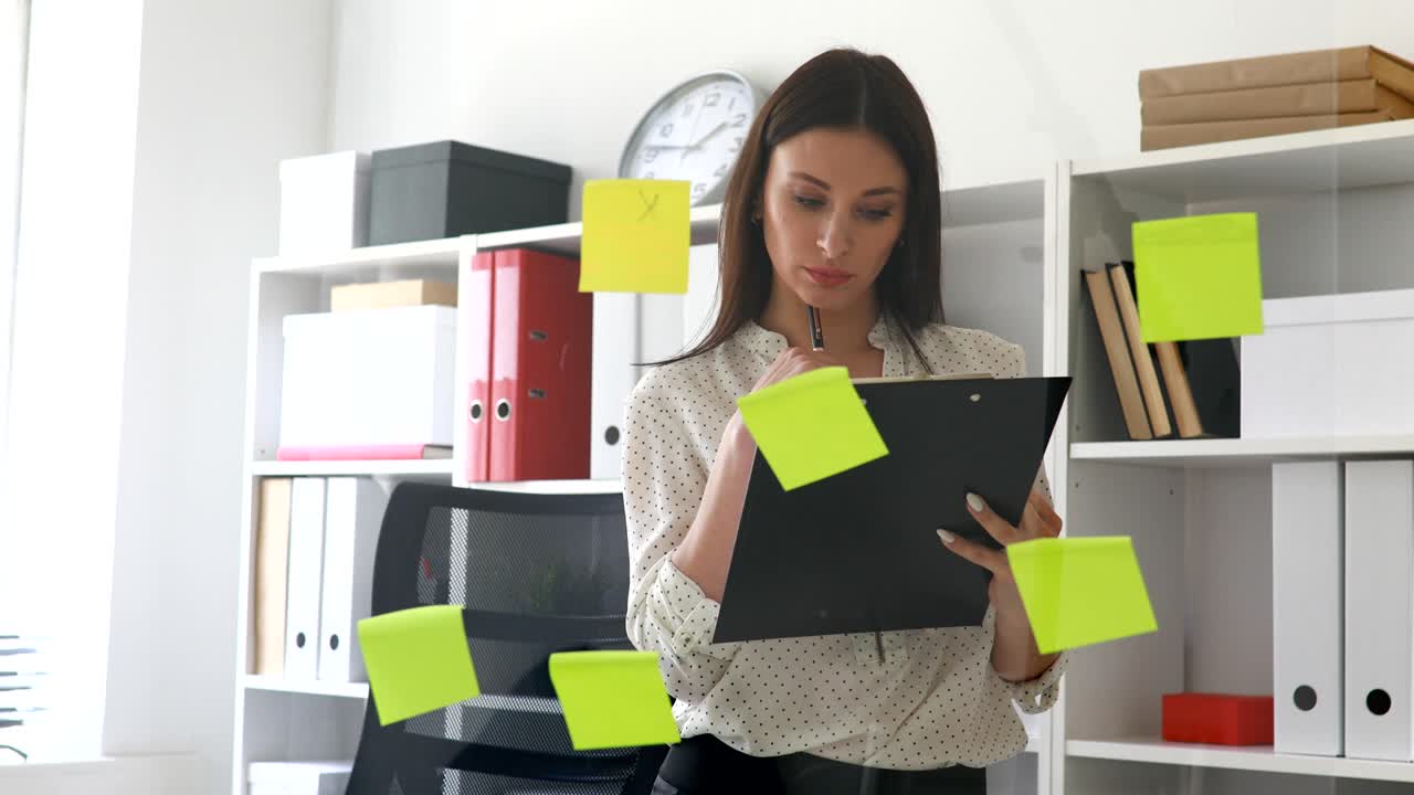 mujer de negocios haciendo notas en documentos de pie cerca de la pared de vidrio