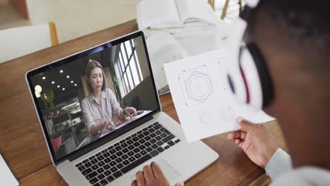 African-american-businessman-sitting-at-desk-using-laptop-having-video-call-with-female-colleague