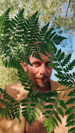 man in a beige jacket behind ferns