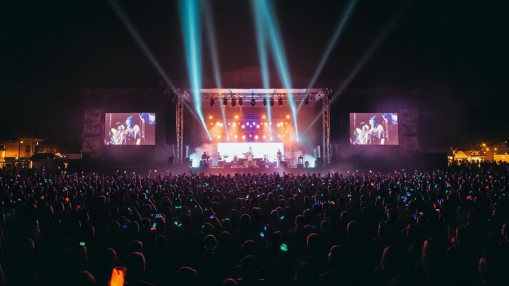 Un'entusiasmante scena di un concerto notturno con una folla immensa, giochi di luce colorati e interpreti affascinanti sul palco che creano un'esperienza indimenticabile