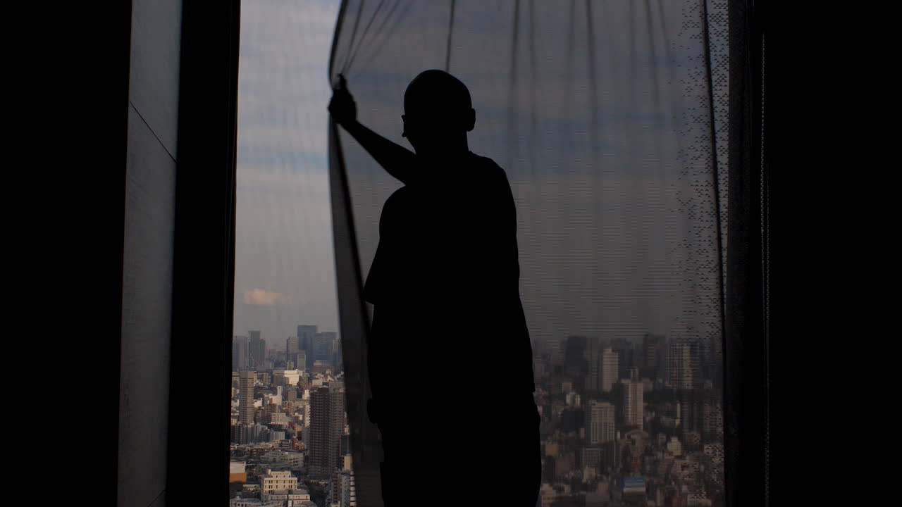 Silueta de un hombre mirando por la ventana, cerrando las cortinas, ocultando la vista panorámica de la metrópolis.