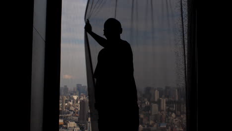 Silhouette-Eines-Mannes,-Der-Aus-Dem-Fenster-Schaut,-Die-Vorhänge-Zuzieht-Und-Den-Panoramablick-Auf-Die-Metropole-Verdeckt