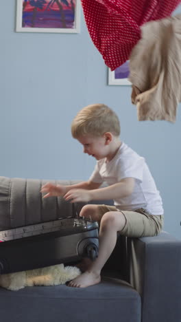 naughty little children throw gathered clothes out of open suitcase in living room. playful boy and girl have fun messing with apparel at home