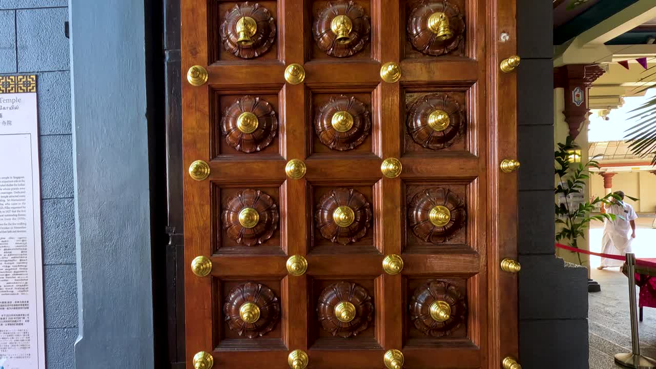 Camera pans upward as intricately carved wooden temple door slowly opens, revealing interior details
