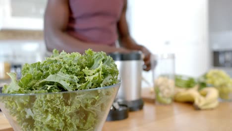 Sección-Media-De-Un-Hombre-Afroamericano-Preparando-Batidos-Saludables-En-La-Cocina-De-Casa,-Cámara-Lenta