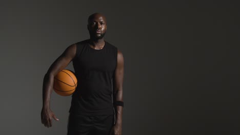 Studioporträtaufnahme-Eines-Männlichen-Basketballspielers,-Der-Den-Ball-Unter-Dem-Arm-Vor-Dunklem-Hintergrund-Hält-2