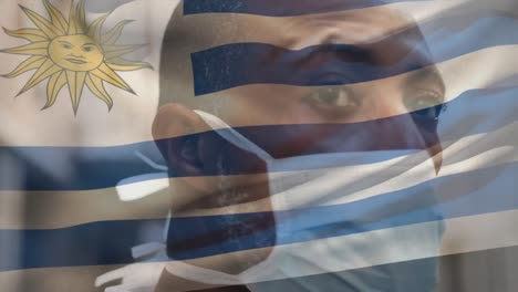 Animation-of-flag-of-uruguay-waving-over-african-american-man-wearing-face-mask-in-city-street