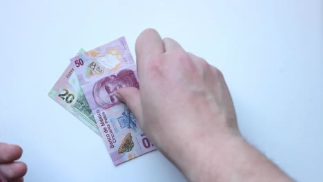 a person putting several mexican banknotes on a clear table. concept: mexican economy