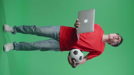cuerpo lleno de hombre asiático con una pelota se arrepiente de animar el fútbol en una computadora portátil en el estudio de pantalla verde