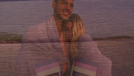 Embracing on beach, couple with flags overlay on wooden texture background