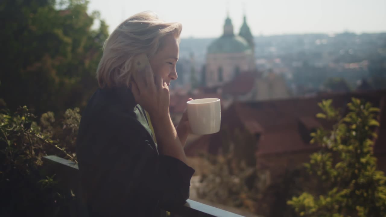 뜨거운 커피 한 잔을 마시면서 전화 통화를 할 때 웃는 발코니에 사업가