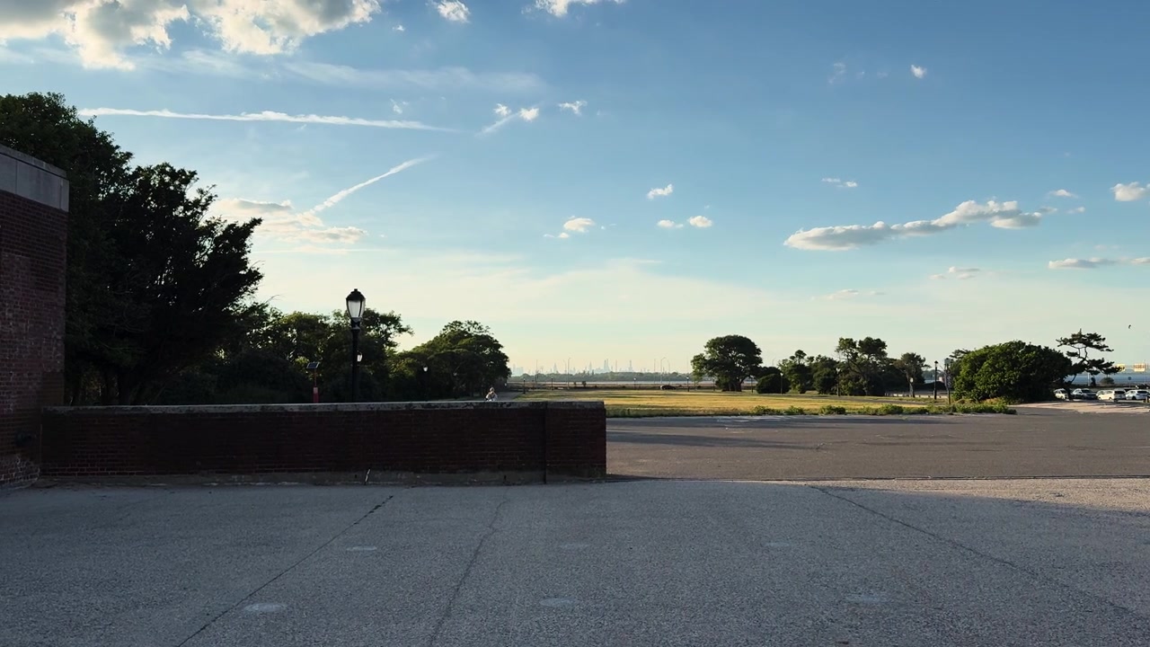 Ampia piazza pavimentata con muro di mattoni, alberi e cielo aperto in una giornata limpida e soleggiata.