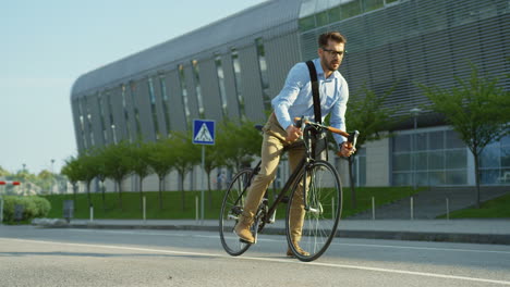 Attractive-young-man-wearing-glasses-and-sitting-on-the-bike-on-the-street-and-looking-at-his-watch