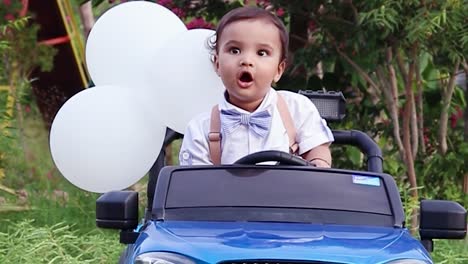 Un-Niño-Pequeño-Aislado-Sentado-En-Un-Coche-De-Juguete-Con-Una-Linda-Expresión-Facial-Al-Aire-Libre