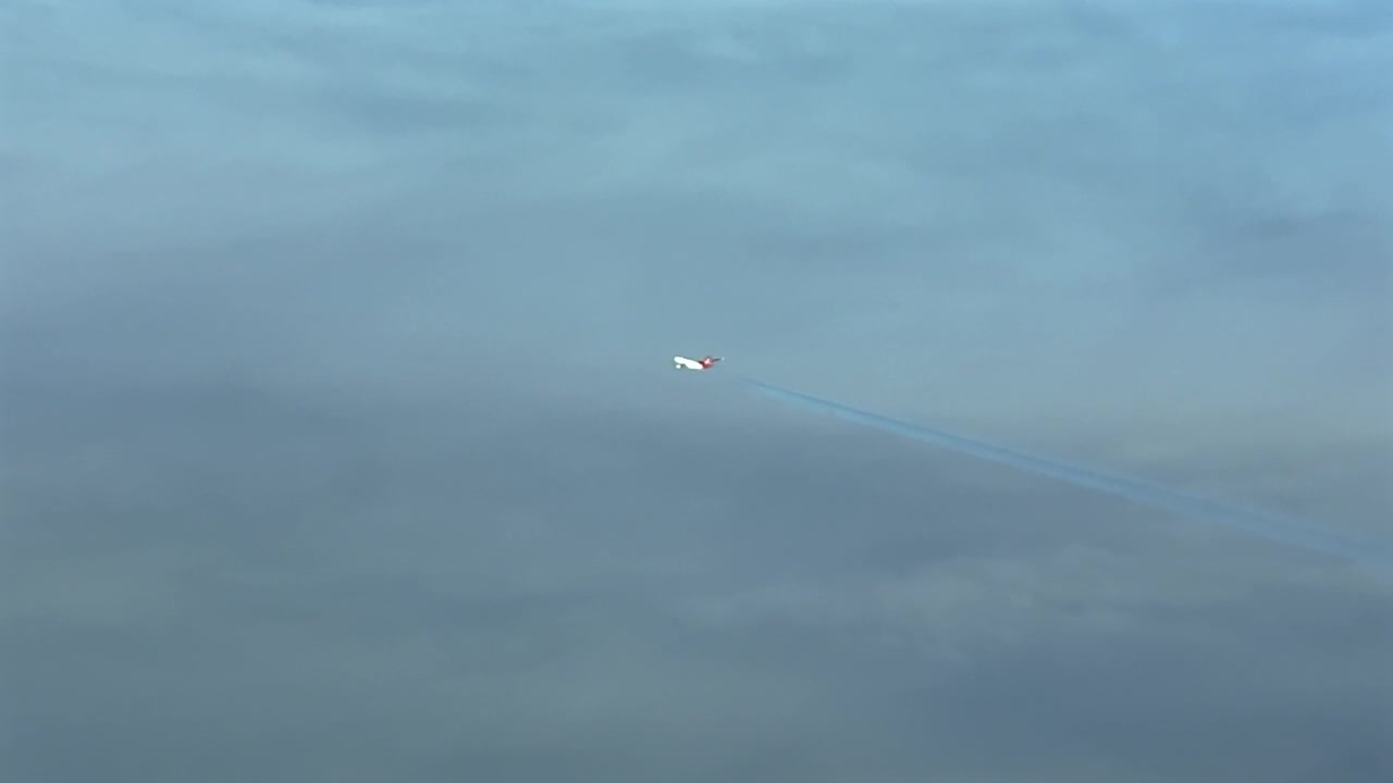 Højre side luftfoto cockpitudsigt af et tomotoret massivt jetfly med en rød hale, der efterlader et falmende kondensspor over et lag af æteriske skyer