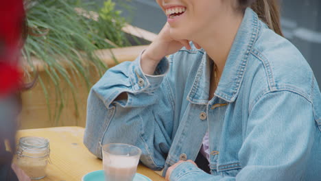 close up of happy same sex female couple meeting and sitting outdoors at coffee shop together