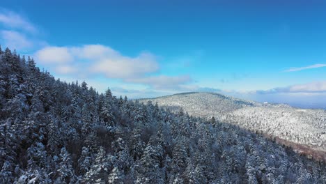 Aerial-footage-flying-around-the-ridge-of-a-snow-covered-mountain-on-a-blue-sky-day