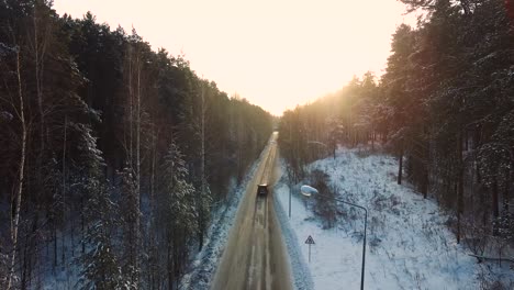 snowy forest road with car at sunrise/sunset