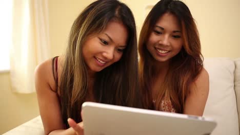 Attractive-sisters-sitting-on-couch-using-tablet