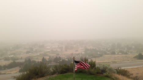 Drohnenaufnahme-Der-US-Flagge,-Die-Mit-Der-Luft-Voller-Rauch-In-Wenatchee-Weht,-Was-Durch-Brände-An-Der-Westküste-Verursacht-Wurde